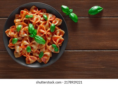 Farfalle, cooked pasta with tomato sauce and basil green leaves, in gray plate, on wooden brown plank tabletop background, top view, space to copy text.
 - Powered by Shutterstock