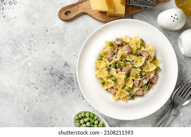 Farfalle With Green Peas, Turkey Ham And Parmesan In Cream Sauce In A White Plate On The Kitchen Table. Traditional Italian Pasta On A Light Culinary Background. Top View	