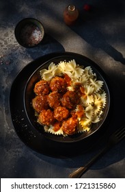Farfalle pasta with chicken meatballs in tomato sauce, on a dark background.