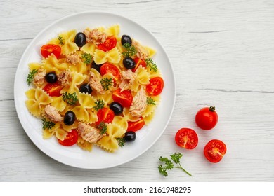 Farfalle pasta salad with canned tuna in olive oil,cherry tomatoes,black olives and parleys on plate with white wood table background.Healthy Italian summer salad.Top view.Copy space - Shutterstock ID 2161948295