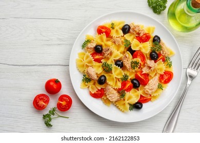 Farfalle pasta salad with canned tuna in olive oil, cherry tomatoes,black olives,parleys,olive oil and peppers on plate with white wood background.Healthy  Italian summer salad.Top view.Copy space - Shutterstock ID 2162122853