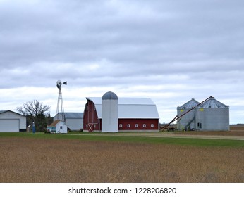 Farm Buildings With Active Windmill On A Cloudy Day In Minnesota - Includes Barn, Granary, Sheds, Bean Field And Grain Auger.