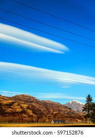 A Farm House At The Foot Of A Hill, With Trees In The Foreground, Mountains In The Background And Lenticular Clouds In The Sky. Taken At Winter, Near The Mt Aspiring National Park NZ