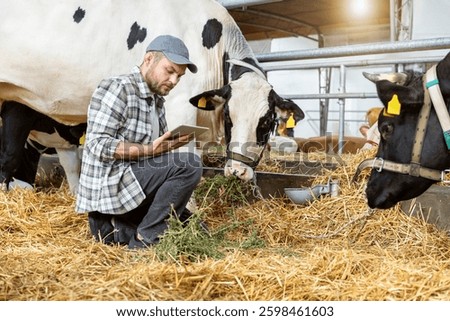 Farm inspector using digital tablet to check cows at livestock farm