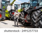 Farm machinery dealer. A man with a digital tablet stands at an agricultural equipment dealer and looks at tractor.