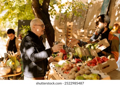 At farm market, friendly african american farmer interacting with senior customer while selling organic vegetables from greenmarket stand. Local vendor selling fresh and healthy produce to elderly man - Powered by Shutterstock