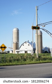 A Farm Next To A Road, A Granary And A Barn, A Power Line Pole, A Planted Field, Against A Blue Sky