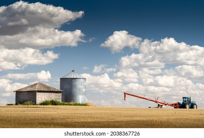 A Farm Tractor And Auger Filling A Grain Silo On A Prairie Wheat Field In Rockyview County Alberta Canada.