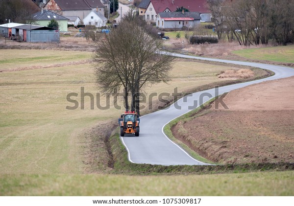 Farm tractor\
is driving on a road in the\
village.