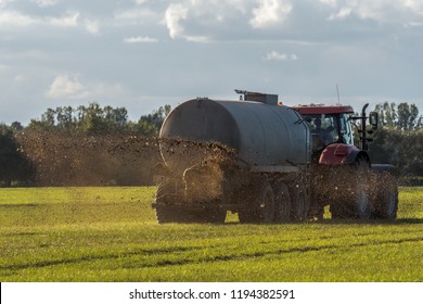 A farm tractor sprays its manure from the tanker onto a field. Manure is used as fertilizer in agriculture. Concept: agriculture