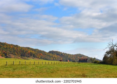 Farm, With Wooden Barn, Sits In Wide Open Field.  Colorful Autumn Trees Decorate The Appalachian Mountains By Farm.