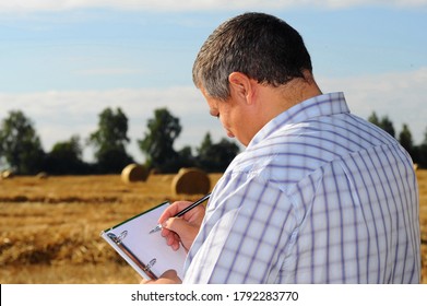 Farmer Agronomist Examines The Field Where The Crop Is Harvested And Makes Notes In His Notebook