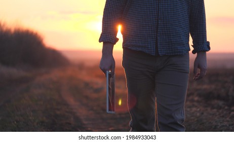 A Farmer In Boots Walks In The Sunset On The Road With A Tablet, The Use Of Modern Gadgets In Agriculture, Work On A Land Farm, Agricultural Work In The Garden, Vegetable Garden Season