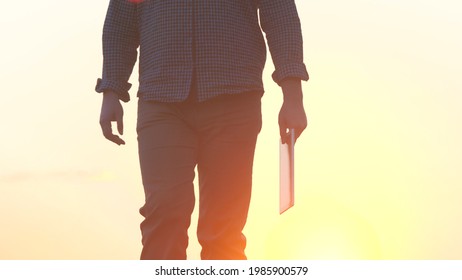 A Farmer In Boots Walks In The Sunset On The Road With A Tablet, The Use Of Modern Gadgets In Agriculture, Work On A Land Farm, Agricultural Work In The Garden, Vegetable Garden Season