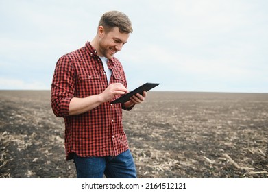 A farmer in boots works with his tablet in a field sown in spring. An agronomist walks the earth, assessing a plowed field in autumn. Agriculture. Smart farming technologies. - Powered by Shutterstock