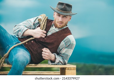 Farmer cowboy wearing hat. Western life. American country male portrait. Farm owner worker in countryside on farm or ranch. Cowboy with lasso rope on sky background.