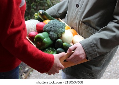 Farmer Delivering A Community Supported Agriculture (CSA) Fresh Produce Box To A Middle Aged Woman