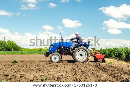 Farmer drives a tractor with a milling machine. Loosens, grind and mix soil on plantation field. Field preparation for new crop planting. Loosening surface, cultivating the land. Farming, agriculture.