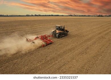 Farmer driving modern yellow crawler tractor harrowing and leveling dry soil for next seeding in rural plain fields, aerial drone shot - Shutterstock ID 2335321537