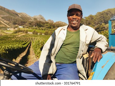 Farmer driving tractor in the fields during harvest in countryside. Vineyard worker sitting on his tractor smiling.
