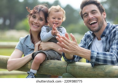 Farmer Family Sitting On Wooden Fence At Farm