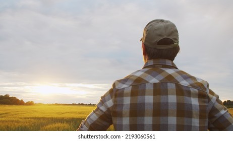 Farmer In Front Of A Sunset Agricultural Landscape. Man In A Countryside Field. Country Life, Food Production, Farming And Country Lifestyle.