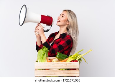 Farmer girl holding a basket full of fresh vegetables over isolated white background shouting through a megaphone