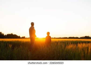 Farmer and his son in front of a sunset agricultural landscape. Man and a boy in a countryside field. Fatherhood, country life, farming and country lifestyle concept. - Shutterstock ID 2260265023