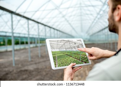 Farmer holding digital tablet with project of the future plantation in the glasshouse - Powered by Shutterstock