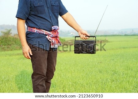 Farmer holds FM-AM radio receiver at paddy field. Concept : Happy working along with music. Country lifestyle. Getting knowledge, information , news , advertisement, songs from listen to radio.     
