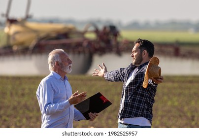 Farmer And Insurance Sales Rep Representative Discussing Arguing. Two Men Agronomist Talking In Field Holding Clipboard Negotiating Standing In Front Of Machinery