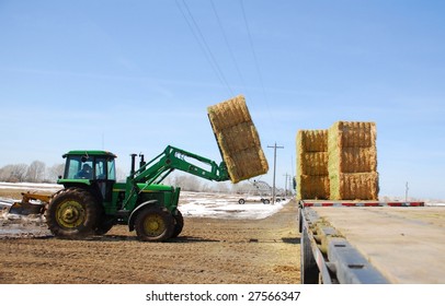 A Farmer Loads A Flat Bed Semi Trailer With Large Bales Of Hay.