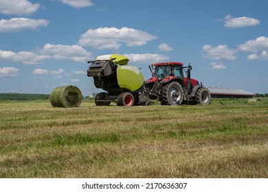 Farmer located in Quebec, Canada is baling hay using a modern round hay baler in the fields. Being hauled by a red tractor, Harvesting hay.  Hay Harvest. Agriculture.  Agricultural machinery.  Farm.