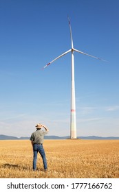 Farmer looking at a huge windmill in his farmland on a sunny day