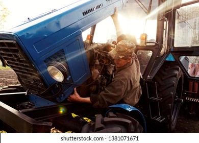 Farmer Mechanic Repairing Blue Tractor Engine. Repair Agricultural Technology At Sunset.