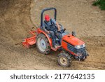 A farmer on a mini tractor loosens the soil for the lawn. Land cultivation, surface leveling.