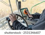 Farmer Operating Auger Joystick in Combine Harvesting Soybeans, Steering Wheel and Tractor Computer Visible in Field, Close-Up of Hand Controlling Farm Equipment During Busy Harvest Season