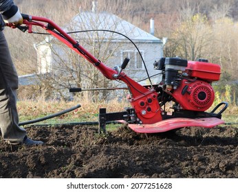 a farmer plows the land with a hand red plow in a rural area, mechanization of heavy manual labor in the cultivation of the land, working with a motor plow in a garden or farm