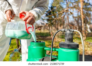Farmer is preparing mixture of water and botanical solutions of pesticide in plastic knapsack sprayer to spray fruit trees in orchard to protect them with chemicals from fungal disease or vermin.