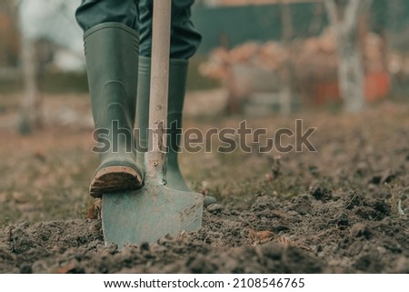 Farmer in rubber boots using spade gardening equipment in garden, low angle, selective focus