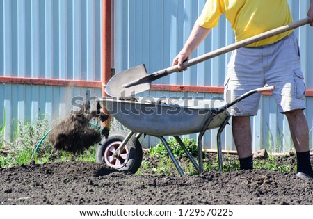 A farmer with a shovel unloads a wheelbarrow filled with earth. Concept - spring field work