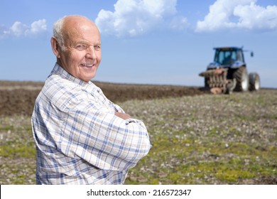 Farmer standing in field with tractor and plough in background - Powered by Shutterstock