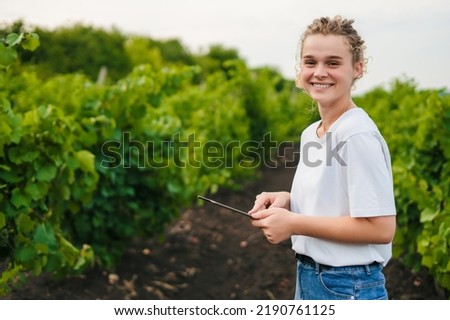 Farmer with a tablet standing in plantation of grapevines, smiling looking at camera, enjoying work time. Free space for text. Smart farming and precision