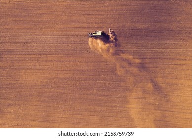 Farmer in a Tractor preparing a field with a seedbed cultivator, Pre seeding activities in early spring season of agricultural works at farmlands. Dry season with draught. Top down view.