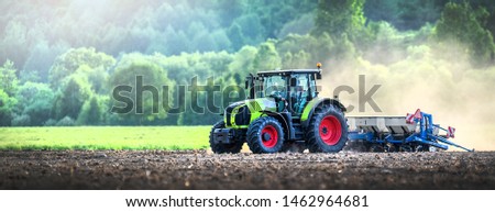 Farmer in tractor is preparing ground or soil with cultivator for seeding activities at spring season. agriculture works and farmland. Wide banner or panoramatic photo.