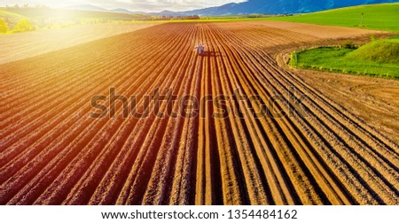 Farmer in tractor preparing land with seedbed cultivator in farmlands. Tractor plows a field. Agricultural work in processing, cultivation of land. Furrows row patter.aerial photo