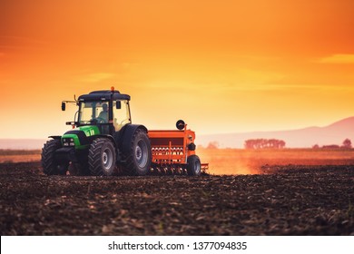 Farmer with tractor seeding crops at field on sunset