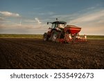 Farmer with tractor seeding - sowing crops at agricultural field. Plants, wheat.