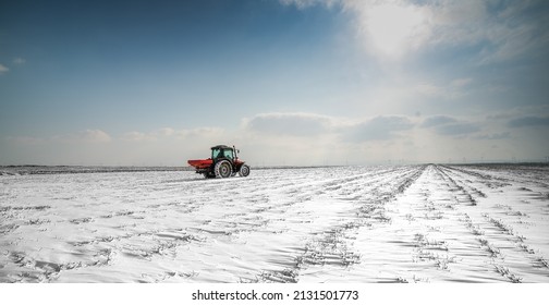 Farmer with tractor seeding - sowing crops at agricultural fields in winter - snow