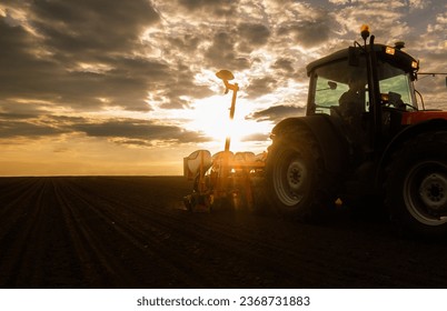 Farmer with tractor seeding - sowing crops at agricultural fields in sunset - Shutterstock ID 2368731883